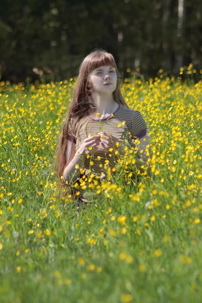 Young woman sits among yellow flowers at meadow at summer day — Stock Photo, Image