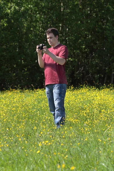 Jonge man houdt camera onder gele bloemen op de weide bij zomer — Stockfoto