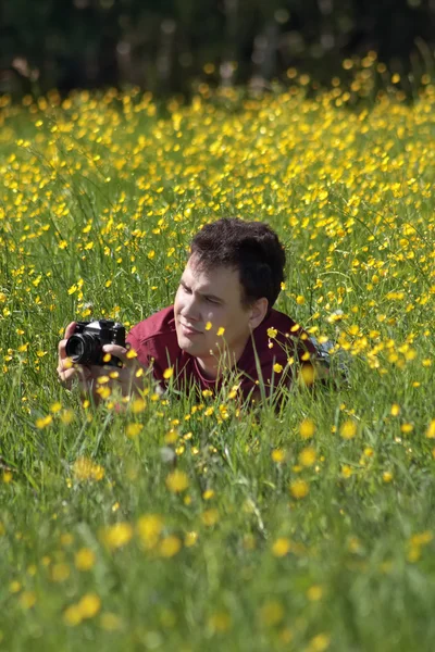 Young man shoots among yellow flowers at meadow at summer day — Stock Photo, Image