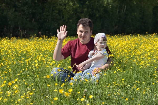 Mladý muž s malou dcerou mezi žlutými květy na louce na — Stock fotografie