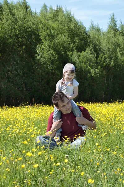 Pai feliz com sua filha em ombros entre flores amarelas — Fotografia de Stock