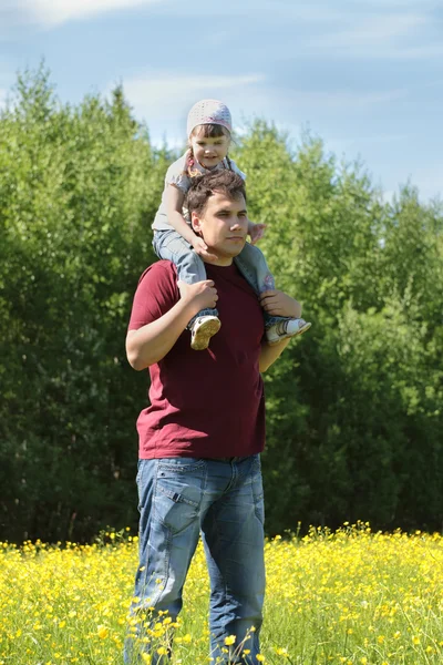 Man with little daughter on shoulders among yellow flowers at me — Stock Photo, Image