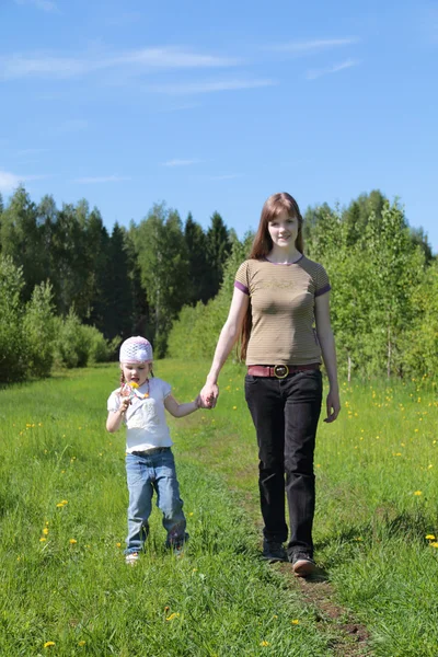 Young woman walks with daughter near green forest at summer day — Stock Photo, Image