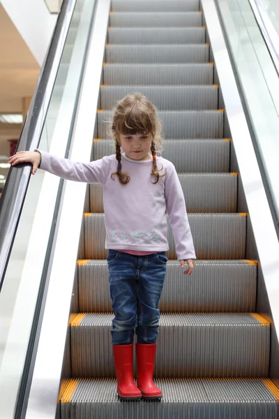 Pretty girl in red gumboots down on escalator in shopping center — Stock Photo, Image