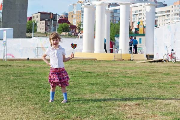 Feliz niña en falda sostiene piruleta en hierba al aire libre — Foto de Stock