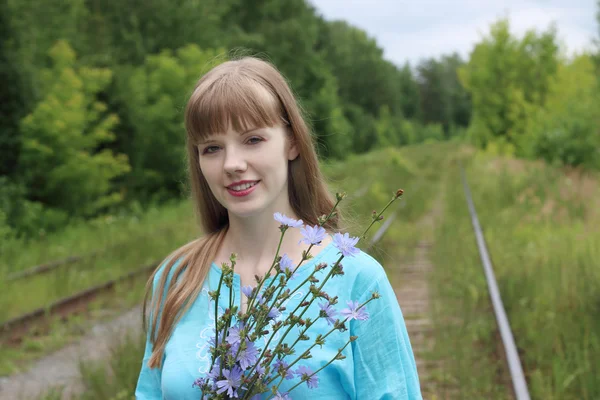 Hermosa mujer en azul sostiene flores de achicoria y sonrisas —  Fotos de Stock