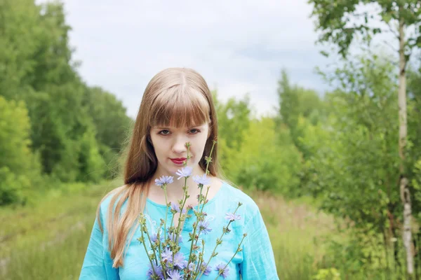 Hermosa mujer en azul sostiene flores de achicoria y sonrisas — Foto de Stock