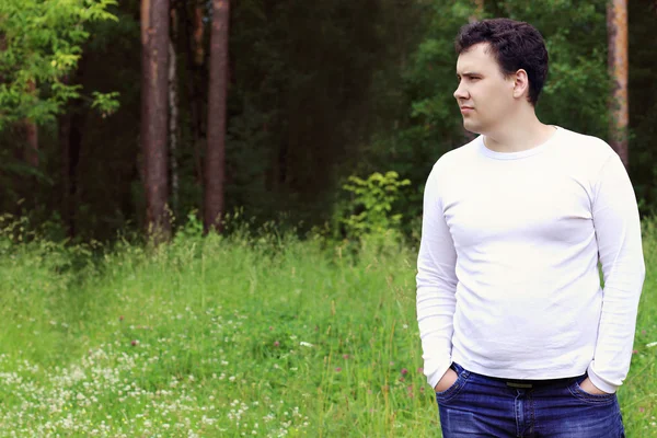 Handsome man in white stands in forest and looks away at summer — Stock Photo, Image