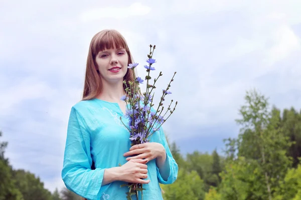Mujer bonita en azul sostiene flores de achicoria y sonríe en verano Imágenes de stock libres de derechos