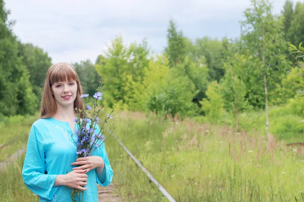 Mujer bonita en azul sostiene flores de achicoria y sonrisas Fotos de stock