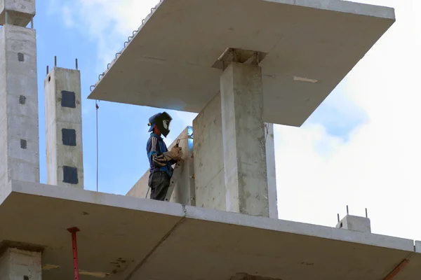 El hombre en la construcción de soldaduras máscara permite gran edificio de apartamentos Imagen de archivo