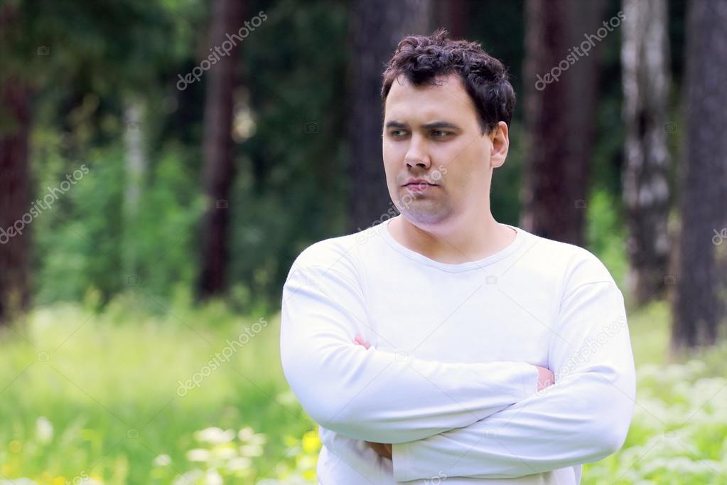 Young handsome man in white looks away and thinks in summer