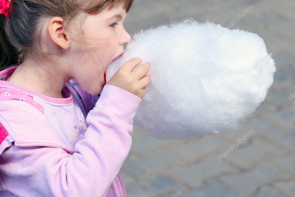 Little beautiful girl in pink eats cotton candy outdoor