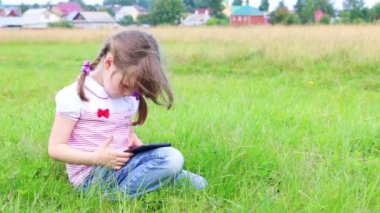 Küçük kız oturur ve yeşil çayır köyü yakınlarında, tablet pc ile çalış