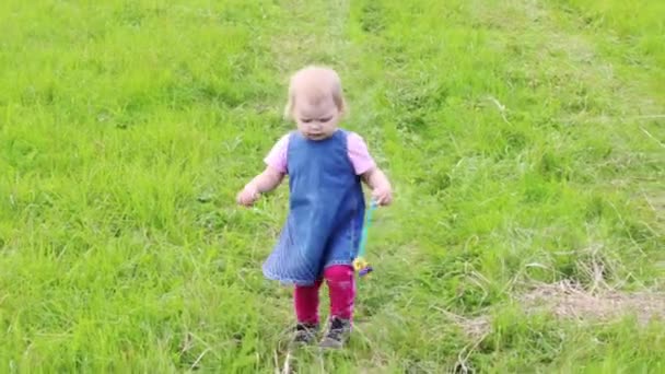 Klein schattige blonde meisje in jurk gaat op groen gras op zomer — Stockvideo