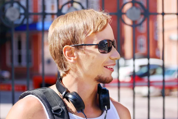 Beau jeune homme aux lunettes de soleil et aux écouteurs sourit — Photo