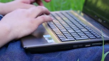 Dizüstü bilgisayarda yazarak ve bahar çimenlerin üzerinde oturan bir adam elinde