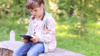 Küçük şirin kız taş duvarda oturur ve tablet Pc Park ile çalış