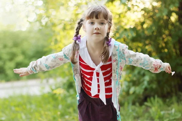 Pretty smiling little girl with braids depicts bird at summer — Stock Photo, Image