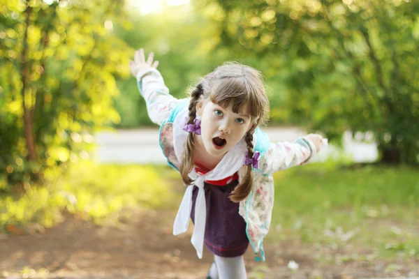 Pretty smiling little girl with braids depicts bird at sunny day — Stock Photo, Image