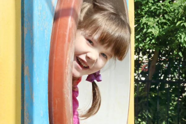 Pretty little girl peeks up of pipe on playground at summer day — Stock Photo, Image
