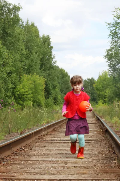 Mooi klein meisje met bal draait op oude spoorlijn tussen bomen — Stockfoto