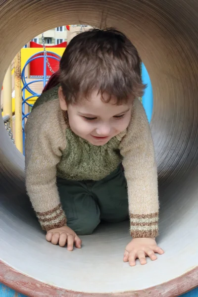 Guapo niño se arrastra en la tubería en el patio de recreo en verano — Foto de Stock