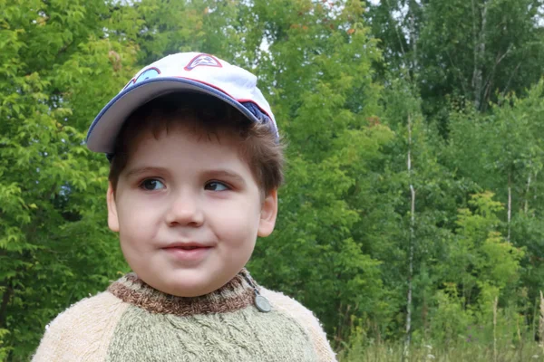Красивый маленький мальчик в шапочке смотрит в сторону в летнем зеленом лесу — стоковое фото
