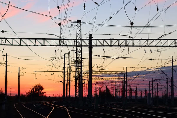 Järnvägen fodrar i mörkret under rosa solnedgång och stolpar — Stockfoto