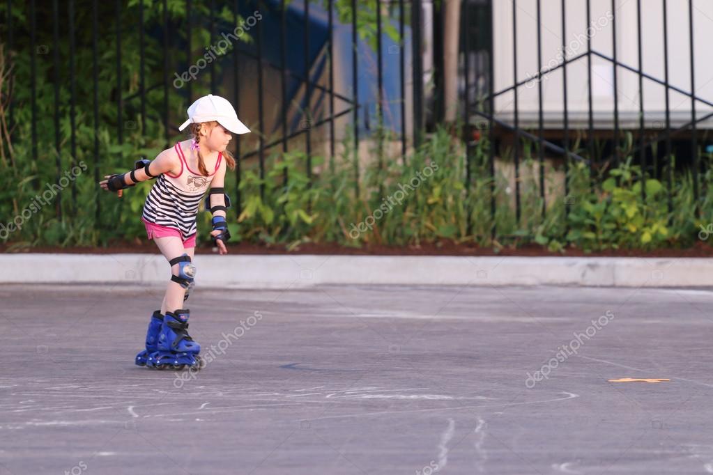 Happy little girl in shorts roller skates on asphalt in summer Stock