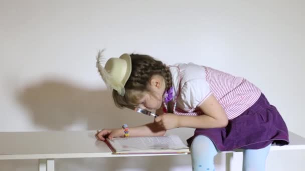 Little girl reading book sitting on table with magnifying glass — Stock Video