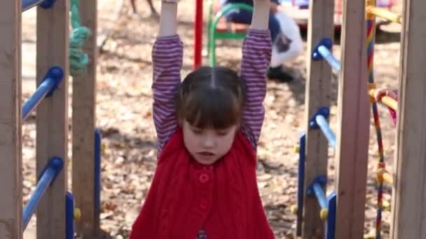 Kleines Mädchen in roter Weste spielt am Herbsttag auf Spielplatz — Stockvideo