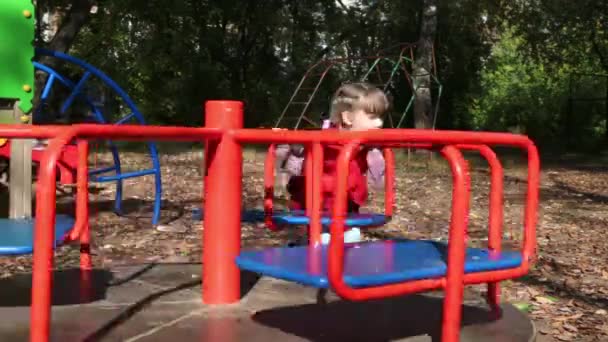 Kleines Mädchen in roter Weste schiebt an einem Herbsttag ein leeres Karussell — Stockvideo