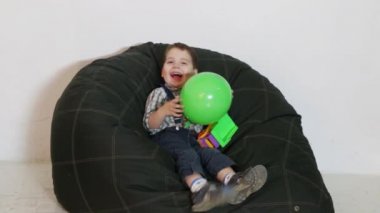 Topu elinde ile yumuşak çanta üzerinde oturan sevimli küçük çocuk