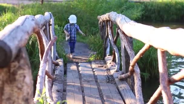 Pequeño descalzo chico en gorra va en hermosa madera puente — Vídeos de Stock