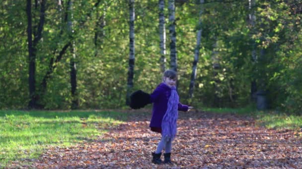 Niña con abrigo ondea su mano y gira en el día de otoño — Vídeos de Stock