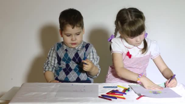 Niño y niña dibujan con lápices de colores sentados a la mesa — Vídeos de Stock