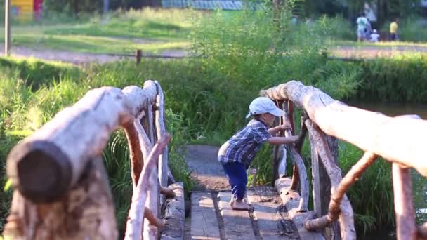 Lindo niño en la tapa juega en hermoso puente de madera — Vídeos de Stock