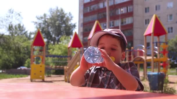 Menino na água potável do boné no dia ensolarado do verão — Vídeo de Stock