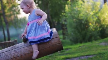 Tahta salıncakta elbiseli sarışın saçlı küçük şirin kız rides