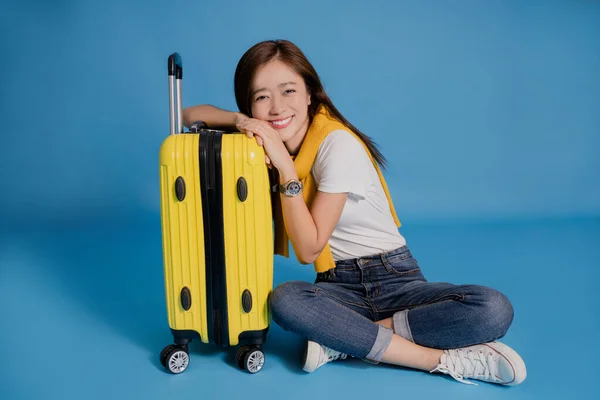 Young Asian tourists smiling in casual clothes. She is sitting near the suitcase on a blue background.