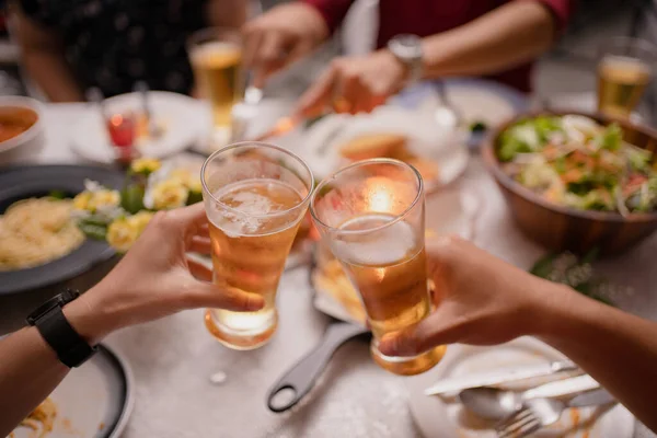 Asians are at a party and drinking beer at home. They clink glasses of beer