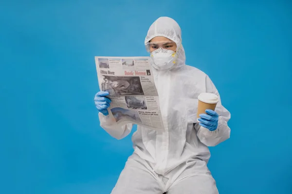 手袋とマスクで保護スーツのアジアの医師 彼女は新聞とホットコーヒーを手に取って読んでいる — ストック写真