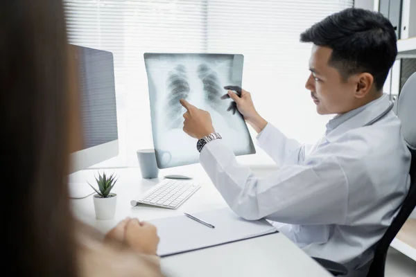 Expert doctor is examining and explaining the x-ray film to the patient.