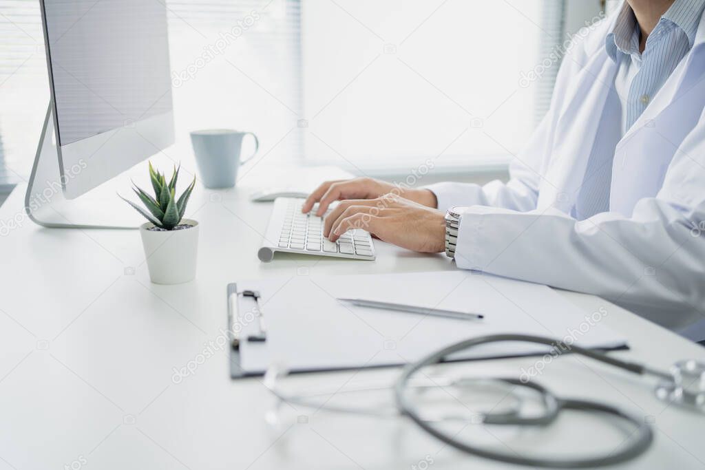 Doctor was sitting and working with the computer on the table in the office.