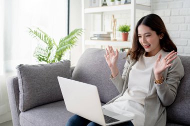 Güzel genç bayan dizüstü bilgisayar kullanıyor ve iyi haberler yüzünden heyecanlandı. Evdeki kanepede oturuyor..