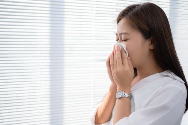 Asyalı kadın kendini hasta ve hapşırık gibi hissediyor. Evde ağzını kapatmak için mendil kullanıyor..