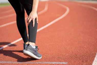 Genç bir Asyalı kadın koşucu, dışarıda koşarken bacağından yaralanmış. Bacağı ağrıyor..