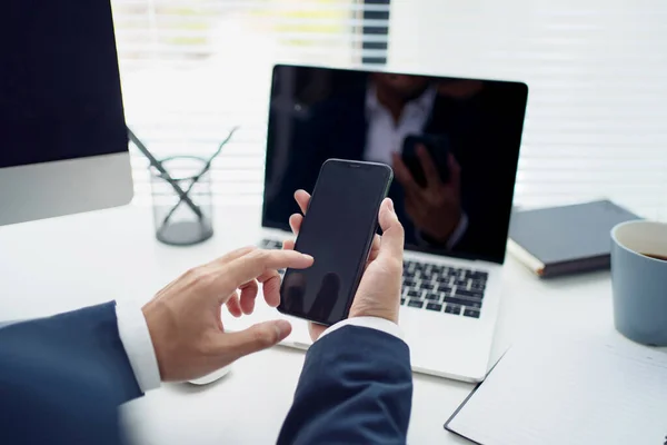 Close-up of a young Asian businessman\'s hand holding mobile phone and touching screen on desk in an office. Social networks and business concept.