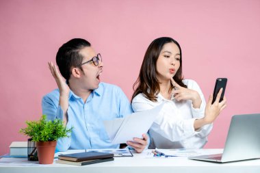 Güzel bir kadın akıllı telefonuyla selfie çeker ve genç bir erkek kendini tatminsiz hisseder ve azarlar. Elinde belgeler var. Birlikte çalışmak kavramı. Pembe arka planda izole edilmiş..